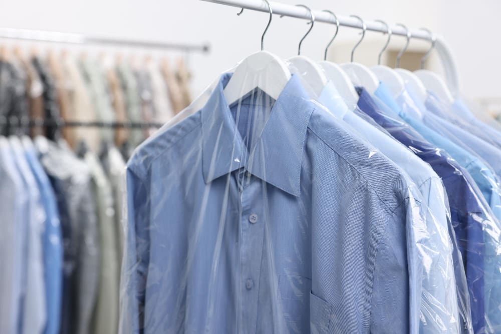 Several blue dress shirts on hangers are covered with clear plastic garment bags, hanging on a rack in what appears to be a Dry cleaning Syracuse facility.