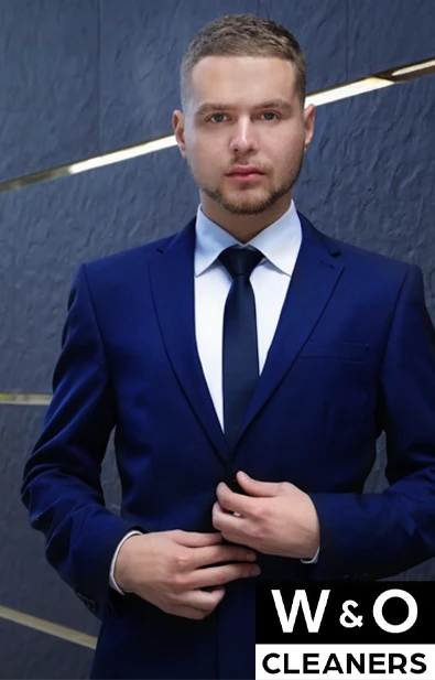 A man in a blue suit and tie stands against a textured dark background. The W & O Cleaners logo is displayed in the bottom right corner.