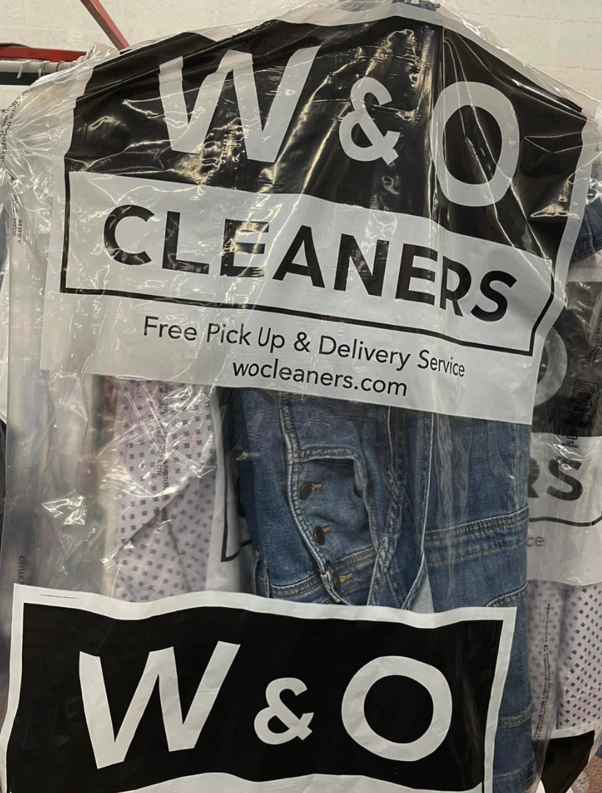 Clothes covered in a plastic bag with the W&O Cleaners logo and a sign offering free pick up and delivery service.